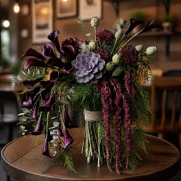 Dark purple floral arrangement with calla lilies and a succulent centerpiece