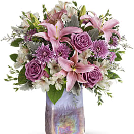 Pink lilies and lavender roses with white blooms in a tall iridescent vase