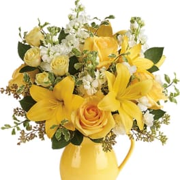 Yellow lilies and roses with white blooms arranged in a yellow ceramic pitcher