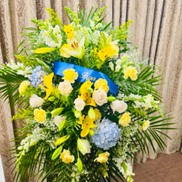 Large standing floral arrangement with yellow lilies, white roses, and blue hydrangea