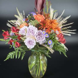 Mixed bouquet of lavender roses, orange mums, and red flowers in a glass vase