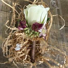 White rose boutonniere with purple flowers in a clear plastic box