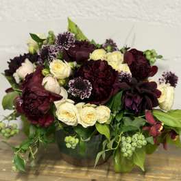 Bouquet of burgundy and cream roses with dark blooms in a vase