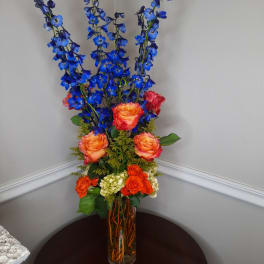 Tall bouquet of blue flowers and orange roses in a glass vase