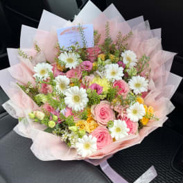 Pink and white mixed bouquet with daisies and roses wrapped in pale pink paper