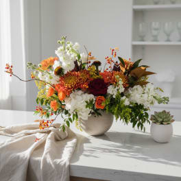 Autumn floral arrangement in a white vase with orange, white, and burgundy blooms
