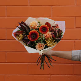Handheld bouquet of peach roses and orange flowers wrapped in white paper