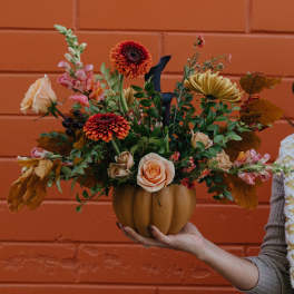 Autumn floral arrangement in a pumpkin-shaped vase with roses and mums