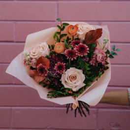 Bouquet of blush roses, pink blooms, and dark purple flowers wrapped in pale paper