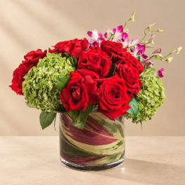 Red roses with green hydrangeas and pink orchids in a glass vase