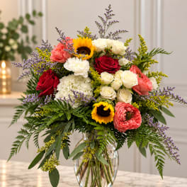 Mixed bouquet of roses, sunflowers, and hydrangea in a glass vase