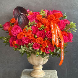 Pink and orange rose arrangement in a pedestal vase with dark decorative pods