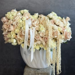 Large cream and blush rose arrangement in a white vase with trailing dried accents