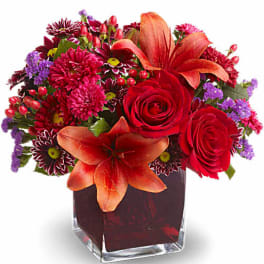 Red and orange mixed flower arrangement in a square glass vase