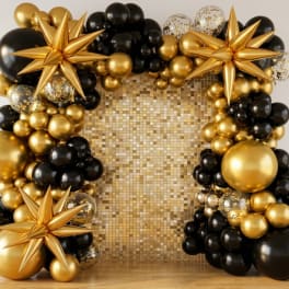 Gold and black balloon arch with starburst decorations around a gold backdrop