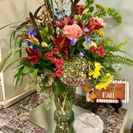Tall mixed bouquet in a glass vase with roses, lilies, and bright fall colors
