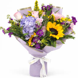 Bouquet of sunflowers, hydrangea, roses, and purple flowers wrapped in lavender paper