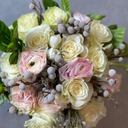 Round bouquet of cream roses, blush ranunculus, and gray berries in a tight clustered design