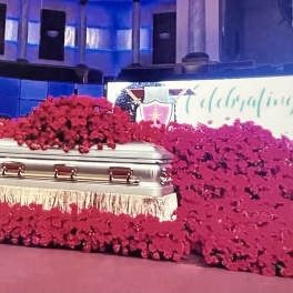 Silver casket surrounded by large red floral sprays