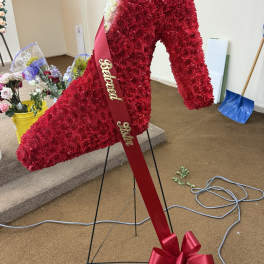 Large red floral funeral wreath on a stand with a ribbon