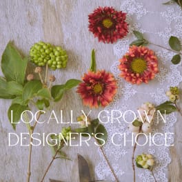 Flat lay of red daisy-like blooms, berries, and foliage on wood with text about locally grown designer’s choice.