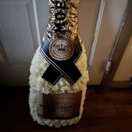 White floral champagne bottle arrangement with black ribbon and gold foil wrap