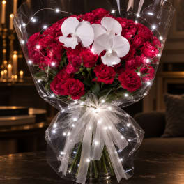 Red carnation bouquet with white orchids wrapped in clear cellophane and a white bow