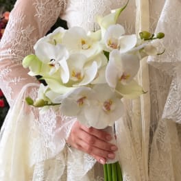 Bride holding a white orchid bouquet against a lace wedding dress