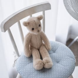 Small beige teddy bear sitting on a blue polka dot chair cushion