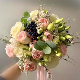 Handheld bouquet of blush and white roses with berries and round greenery