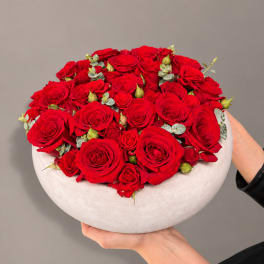 Round arrangement of red roses in a white bowl vase