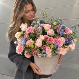 Woman holding a large pastel flower arrangement in a round box