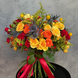 Bouquet of red, orange, and yellow roses with blue thistle and a red ribbon