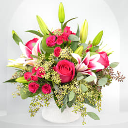 Pink roses and white lilies arranged in a white vase