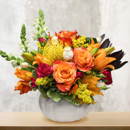 Orange and red mixed bouquet in a round white vase