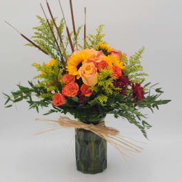 Bouquet of orange roses and sunflowers in a dark glass vase