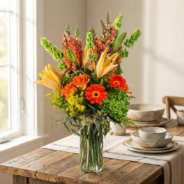 Tall bouquet of orange and yellow flowers in a clear glass vase