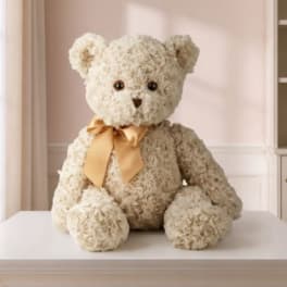 Cream teddy bear with a gold ribbon sitting on a table