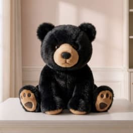 Black teddy bear plush sitting on a white surface