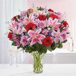 Mixed bouquet of pink lilies, red roses, and lavender flowers in a clear glass vase