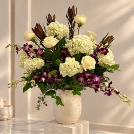 Cream roses and white hydrangeas in a textured vase with purple orchids