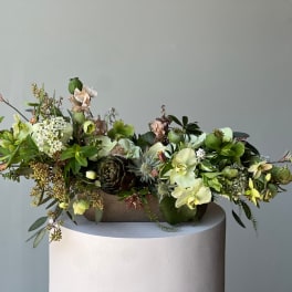 Low floral arrangement with pale green orchids and mixed blooms in a rectangular container