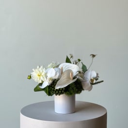 White floral arrangement in a cylindrical vase with orchids and dahlias