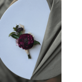 Dark burgundy boutonniere on a white card with gray fabric
