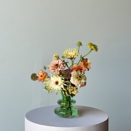 Mixed pastel flowers in a green glass vase on a round pedestal