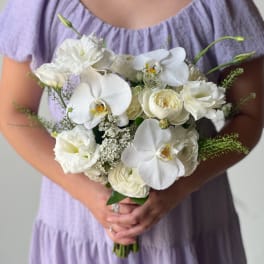 White bouquet with orchids and roses held by a person in a lavender dress
