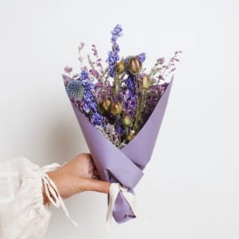 Handheld bouquet of dried purple and blue flowers wrapped in lavender paper