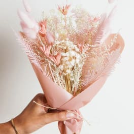 Hand holding a pink dried flower bouquet wrapped in blush paper