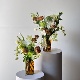 Two floral arrangements in amber glass vases on round pedestals