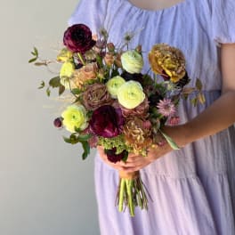 Handheld bouquet of mixed flowers in burgundy, yellow, and blush tones